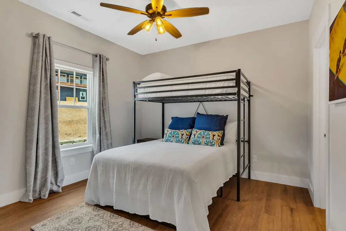 A bright bedroom with a bunk bed, colorful throw pillows, and natural light streaming in from the window. The casual, inviting space feels ideal for relaxing, chatting, or watching movies as a family.