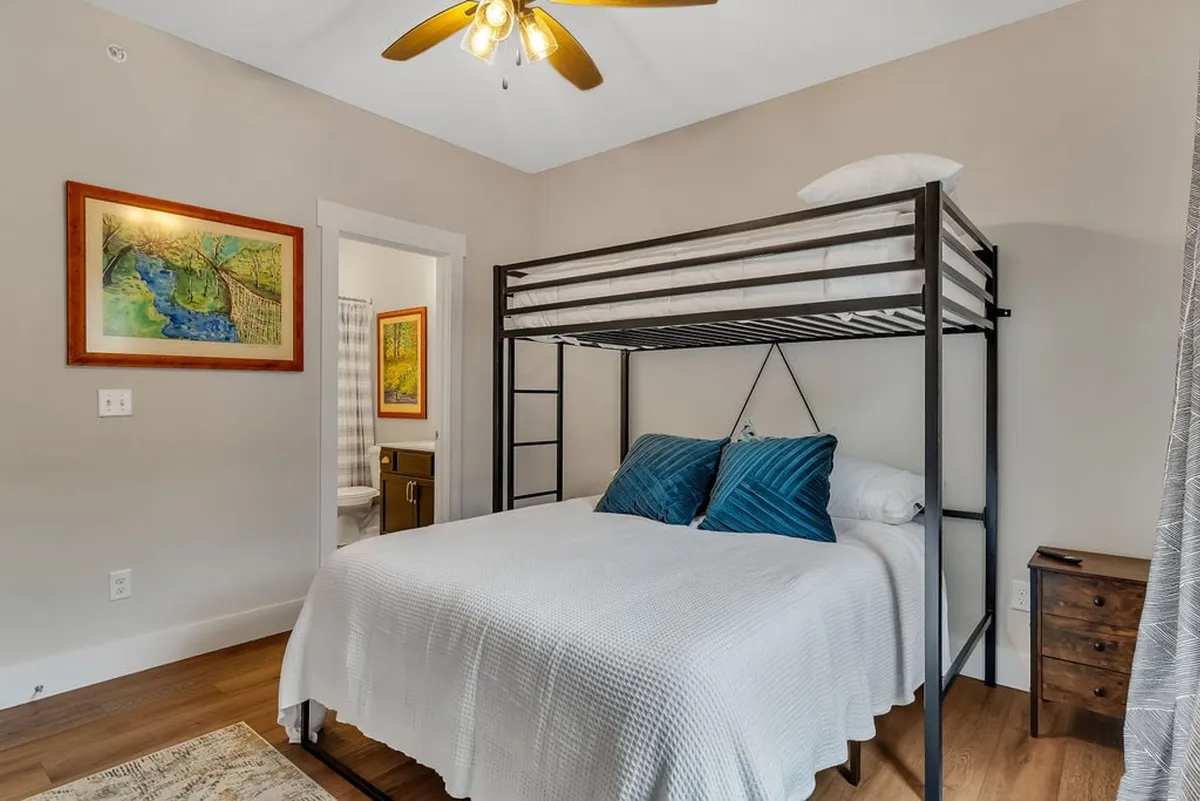 A comfortable bedroom with a bunk bed, plush blue cushions, and cheerful wall art. The bedding setup hints at a twin-over-queen arrangement, creating space for both kids and adults to sleep or lounge together.