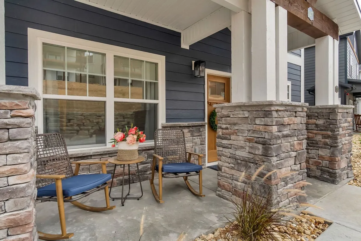 A welcoming front porch framed by stone columns, rocking chairs, and a vibrant flower arrangement. The scene conveys a relaxed, inviting atmosphere and suggests opportunities for outdoor enjoyment, morning coffee, or conversations while taking in the surrounding beauty.