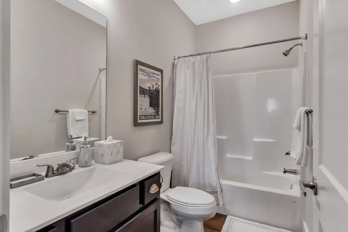 A spacious, modern bathroom with a vanity, large mirror, glass-enclosed shower, and framed artwork. The room is bright, fresh, and perfectly suited for private routines.