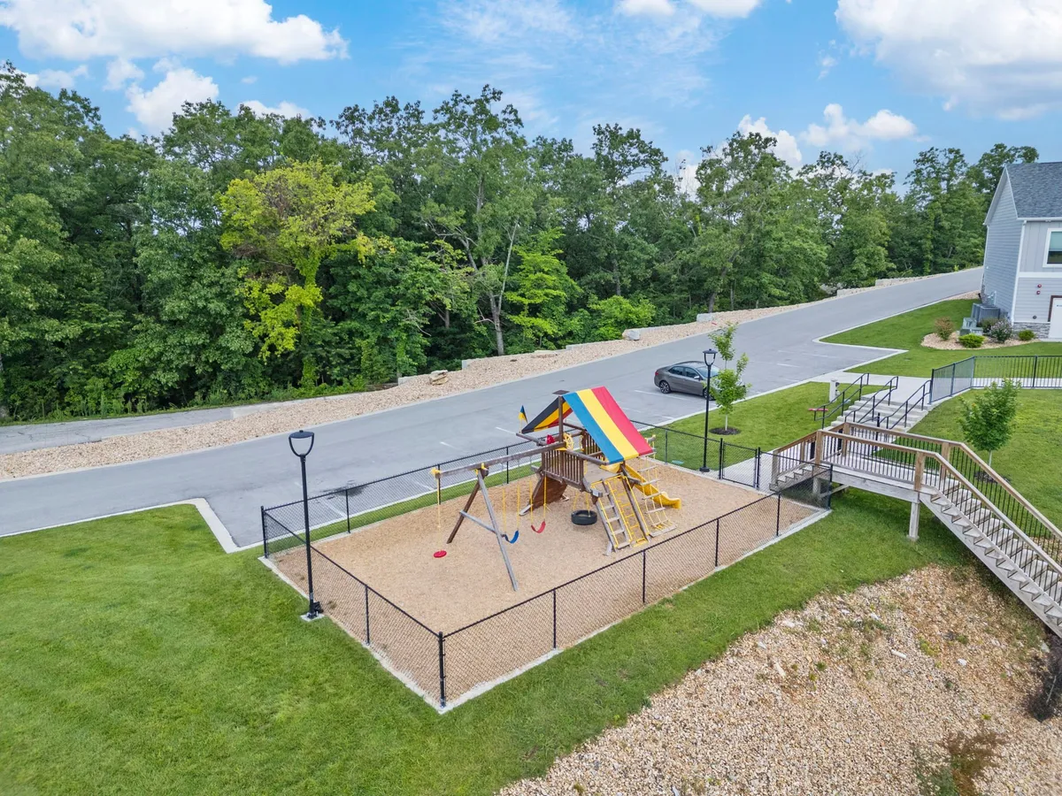 A vibrant outdoor playground area featuring colorful swing sets and a canopy, with children playing and families gathered nearby under the sunshine. The scene radiates a joyful, family-friendly atmosphere and highlights community outdoor amenities.