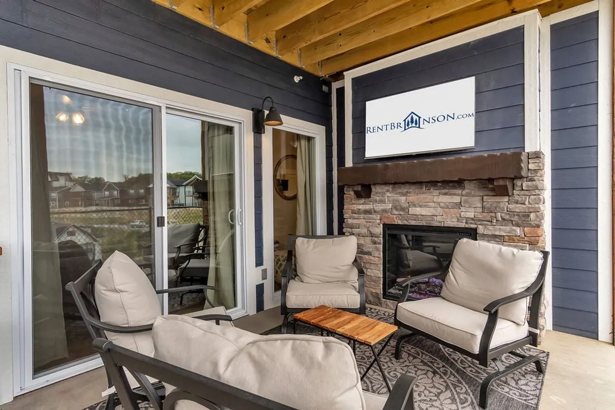 The image showcases the exterior of a spacious, rustic single-family home with a cozy outdoor fireplace surrounded by comfortable seating and a decorative rug. The seating area is designed for relaxation and social gatherings, perfect for enjoying stunning sunset views or unwinding by a crackling fire. The inviting setup hints at year-round enjoyment—whether it's for a summer barbecue or a cozy winter evening.