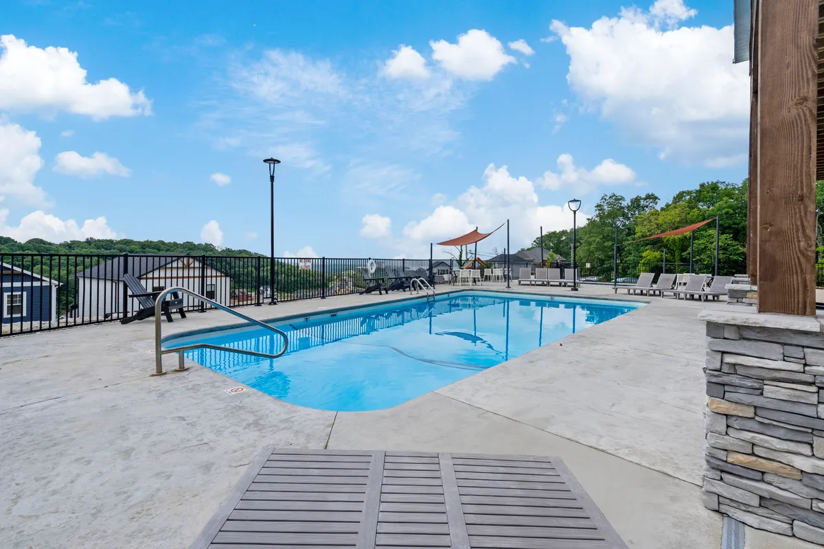 An exterior view featuring a sparkling swimming pool surrounded by lounge chairs and lush landscape greenery, with a scenic backdrop visible. The pool area offers a sense of resort-style leisure and relaxation, inviting guests to swim, sunbathe, and socialize outdoors.