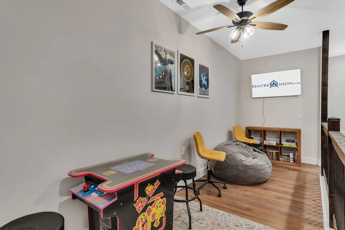 A vibrant, playful loft space featuring an arcade game, a cozy bean bag chair, colorful wall art, and a large television. The room exudes an energetic and inviting atmosphere perfect for gaming, relaxing, and movie nights.