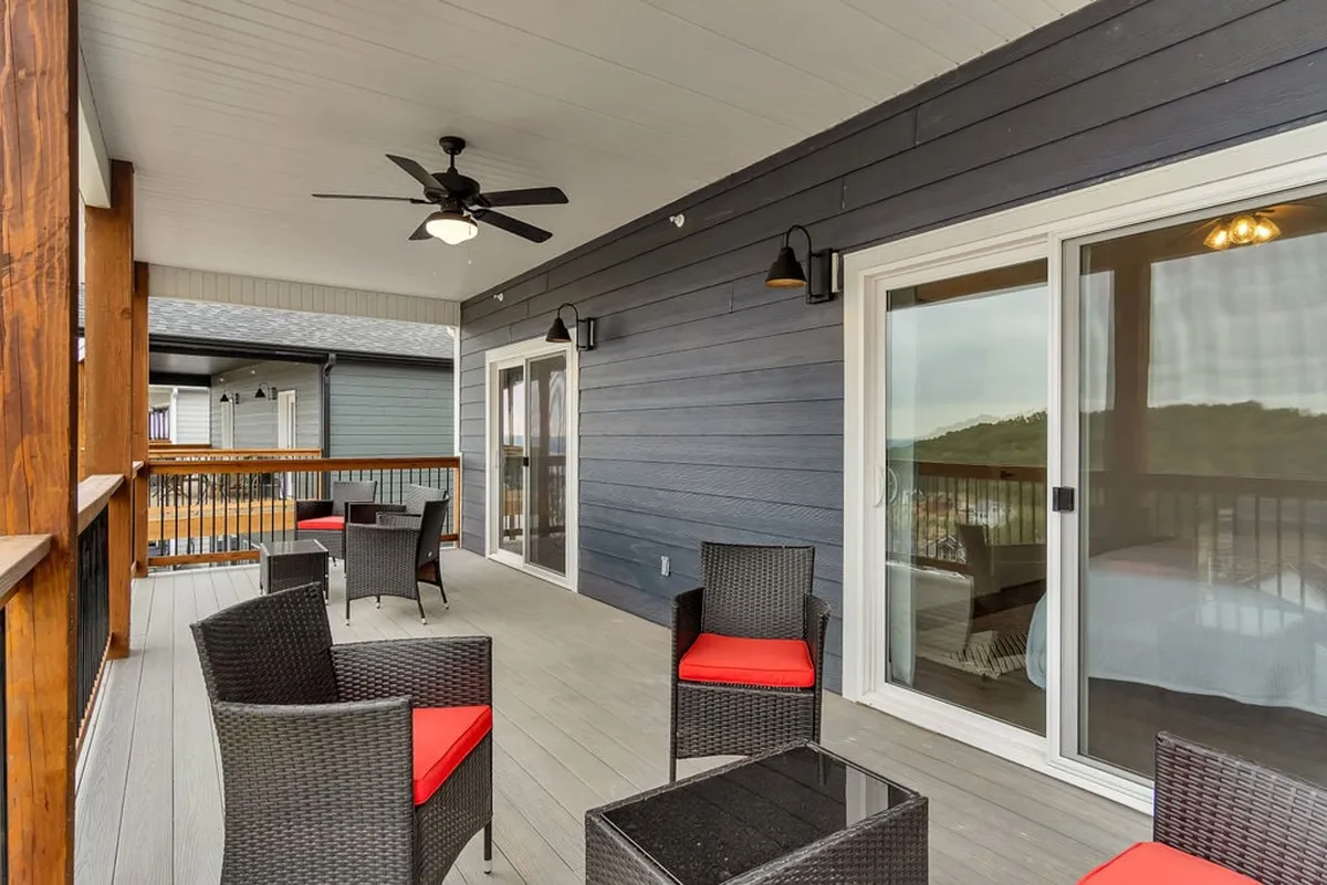 This image features an inviting outdoor seating area on a private patio, complete with comfortable chairs, a coffee table, a ceiling fan, and a view through sliding glass doors. The wooden railing frames the space, while the serene backdrop hints at the peaceful community setting.