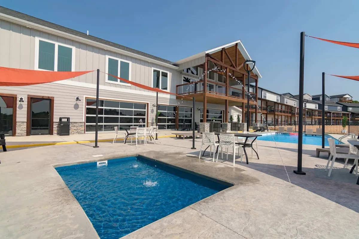 An inviting exterior view of a modern swimming pool, complete with a hot tub and comfortable seating area, set against stylish architecture. The space is designed for socializing, sunbathing, and relaxing poolside.