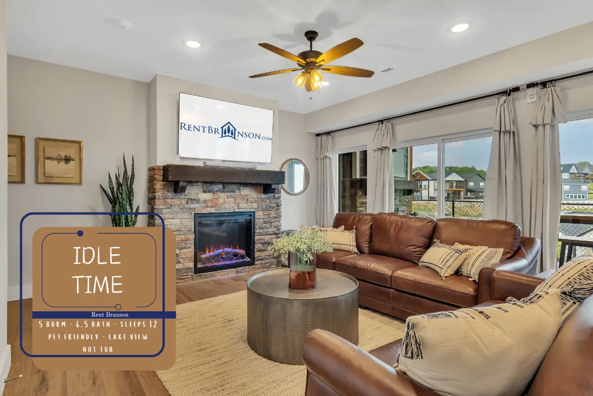 A spacious, welcoming living area featuring a plush brown leather sofa, a coffee table, a cozy fireplace, and large windows that reveal a scenic lake view. The setting is comfortable and ideal for gatherings, relaxation, or watching the sunset together.