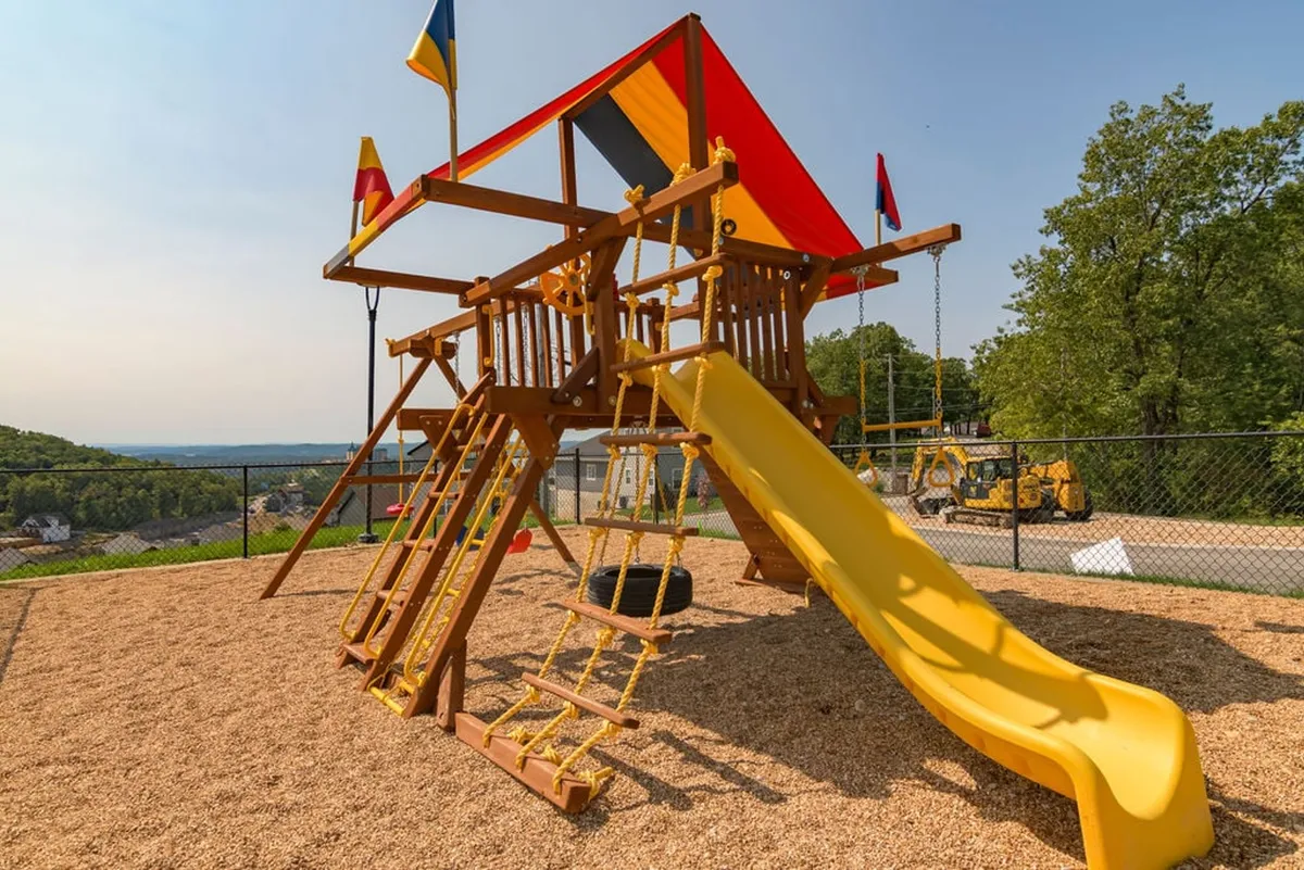 A vibrant exterior playground with a colorful structure, featuring a yellow slide, climbing areas, and festive flags. The area is designed for children and families, suggesting joyful play, social interaction, and family bonding within the community.
