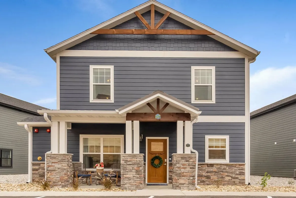 An inviting shot of the main entrance to the property, marked by stone pillars, a decorative wooden beam, and a welcoming wreath on the door. The porch exudes warmth and hints at a community-oriented, neighborly atmosphere.